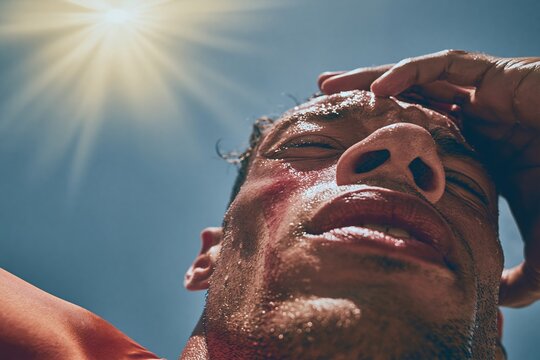 Sweaty man squinting at the sun under a clear sky, showing visible perspiration and skin texture for heat exhaustion and summer wellness concepts