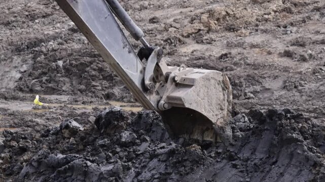 Raw industrial energy and relentless earth-moving force dominate the scene; dark, clumped soil and rugged machinery convey heavy labor and extraction