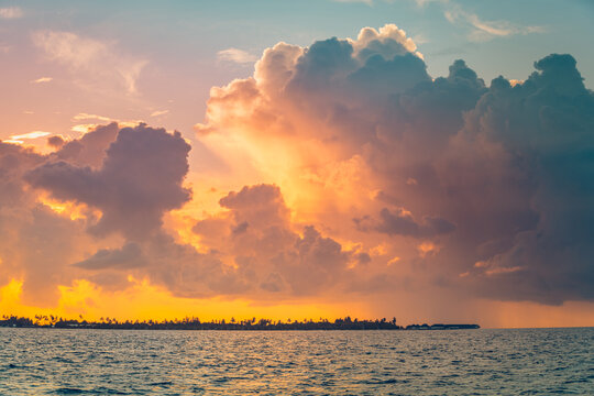 Dramatic weather, sunset glowing golden clouds fiery sky calm ocean tropical island horizon evening. Perfect summer travel landscape paradise. Warm stormy atmospheric coastal scenic wallpaper art