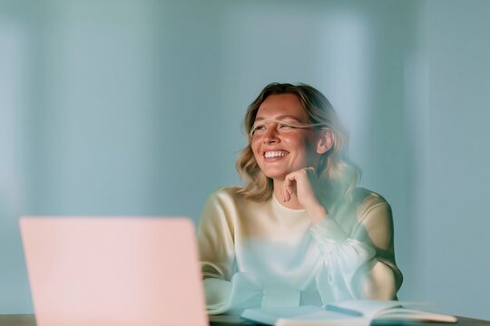 Smiling woman seated at a desk with a laptop and notebook, featuring soft buttery yellow tones and an airy office background for remote work marketing