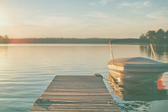 A canopied pontoon boat moored at a weathered timber pier on a still lake, in warm amber evening light for travel and leisure marketing
