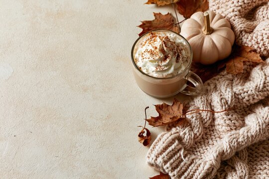 Pumpkin spice latte in a glass mug with whipped cream and cinnamon, surrounded by autumn leaves and a chunky knit sweater for seasonal promotion