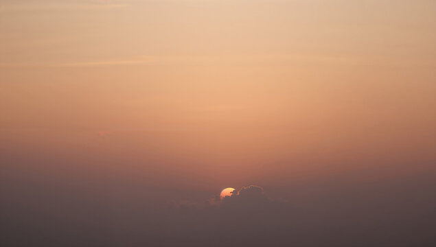 Soft golden sunset sky background with sun rising or setting behind light hazy clouds creating warm pastel orange gradient copy space