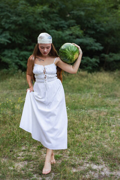Barefoot young woman walking in nature carrying big watermelon on shoulder