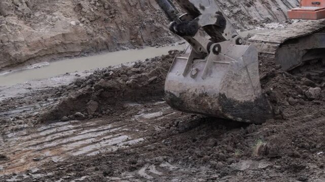 Raw industrial energy and relentless earth-moving force dominate the scene; dark, clumped soil and rugged machinery convey heavy labor and extraction