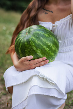 Close up of young woman holding large ripe watermelon on her lap