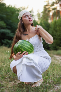 Young woman crouching on green grass and holding large watermelon