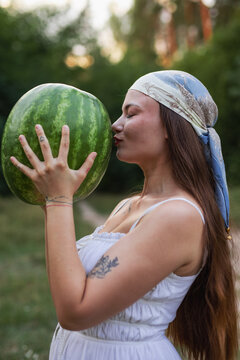 Young woman in headscarf kissing large green watermelon in nature