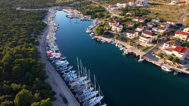 High aerial view of Luka &Scaron;imuni marina on Pag Island, Croatia, with rows of yachts and sailboats moored in a narrow sheltered harbor beside a coastal village and forested peninsula on the Adriatic Sea