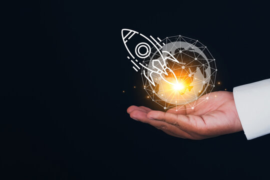 Business startup and global expansion concept. Businessman hand holding a glowing digital wireframe globe with a rocket ship launching graphic on a dark background with empty copy space.