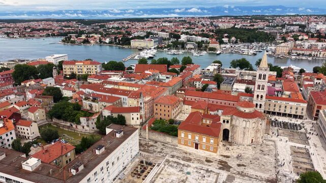 High aerial view of Zadar Old Town in Croatia, showing the historic peninsula with dense red-tiled roofs, church towers, waterfront promenades, marina and the Adriatic Sea surrounding the city center.
