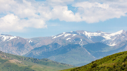 Obraz premium Snow-capped mountains rise behind green rolling hills