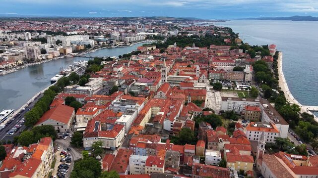 High aerial view of Zadar Old Town in Croatia, showing the historic peninsula with dense red-tiled roofs, church towers, waterfront promenades, marina and the Adriatic Sea surrounding the city center.