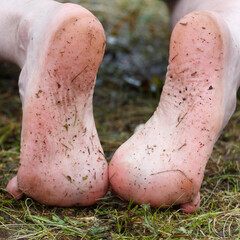 Obraz premium Close-up of bare feet resting on grassy ground. Skin shows natural texture with dirt and plant fragments.