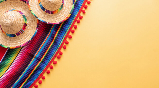 A top-down view of traditional Mexican sombereros and a vibrant serape blanket with red pom-poms on a yellow background, featuring generous copy space.