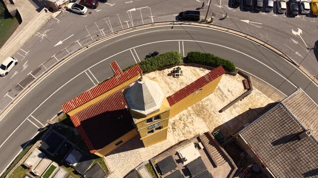 Top-down aerial view of a small historic church in Karlobag, Croatia, beside a curved coastal road with several motorcycles riding past, surrounded by parking areas and traditional red-roofed building