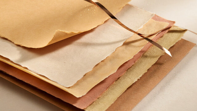 Layered Stack of Textured Handmade Artistic Paper Sheets with Organic Edges and Decorative Copper Ribbon Element for Creative Crafting Projects