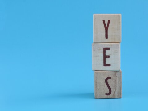 Yes word spelled out with wooden blocks on blue background. Perfect concept for agreement, approval, positive thinking, decision making, success, acceptance, business choices, and customer feedback