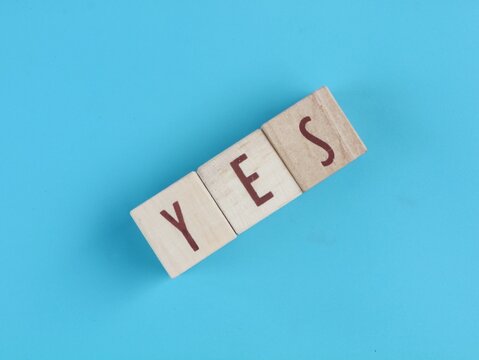 Yes word spelled out with wooden blocks on blue background. Perfect concept for agreement, approval, positive thinking, decision making, success, acceptance, business choices, and customer feedback