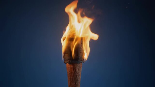 Bright flaming torch burning against dark blue background with intense fire light