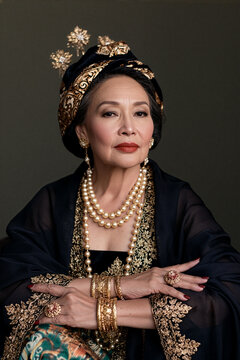 Elegant portrait of a senior Indonesian matriarch in traditional embroidered kebaya and golden jewelry.