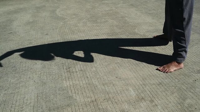 A person standing barefoot casting a long dramatic shadow on a concrete surface. daily outdoor welness activity