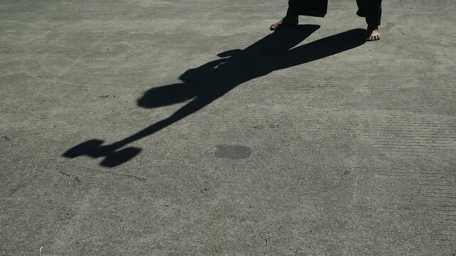 A person casting a long shadow while lifting a heavy dumbbell on concrete. daily outdoor welness activity