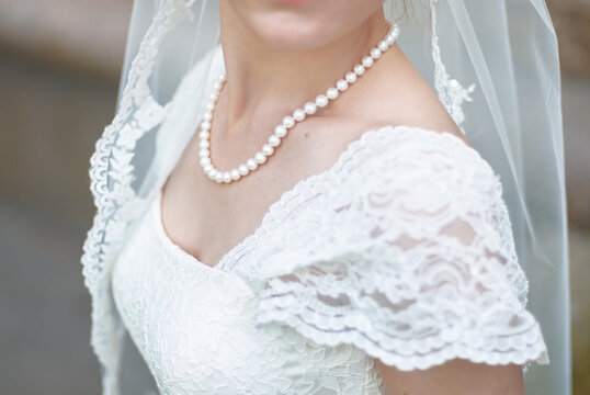 Close-up bridal portrait of a bride wearing a pearl necklace and lace wedding dress with a delicate veil, conveying elegance, romance and timeless wedding style.