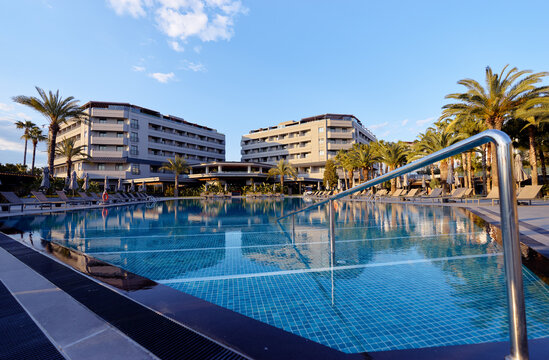 Luxury resort swimming pool with palm trees, lounge chairs and modern hotel buildings under clear blue sky