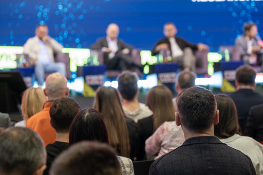 Attendee faces a panel of four speakers during a large business conference session.