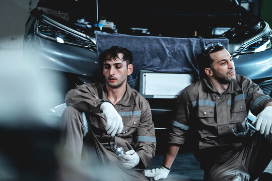 Two Automotive Mechanics Taking a Short Rest Inside a Car Repair Workshop After Completing Demanding Vehicle Maintenance Work