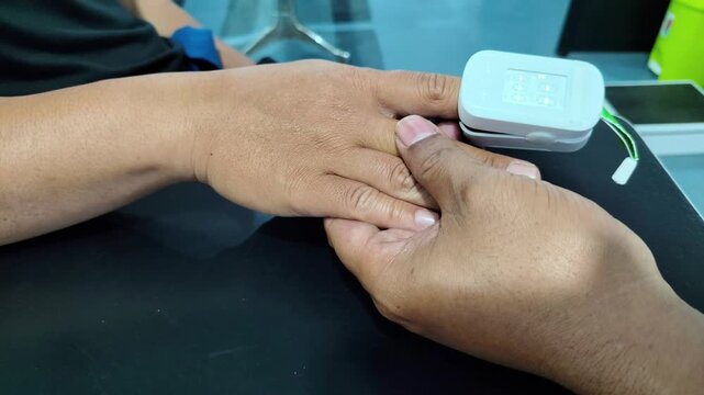 Doctor measuring blood oxygen saturation with pulse oximeter. Close-up of a medical professional attaching a fingertip pulse oximeter to a patient's hand to monitor vital signs, checking oxygen level