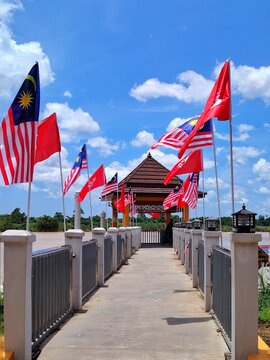 Malaysian national flags known as Jalur Gemilang and Kelantan state flags waving on a concrete jetty under a bright blue sky. Independence day concept in Kelantan, Malaysia