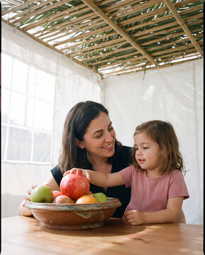 Mother and toddler arranging fruit bowl with pomegranate inside sukkah