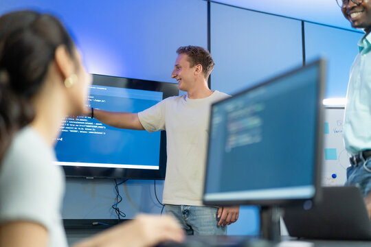 Developer points to and explains code to diverse team members, demonstrating technical knowledge transfer and inclusive group learning through collaborative code walkthrough.