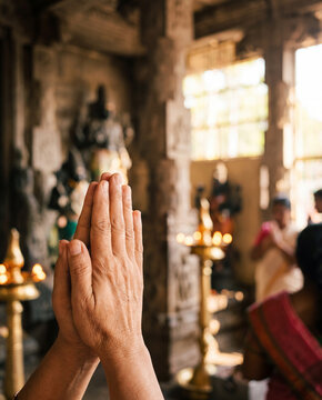Praying hands in namaste gesture inside temple with oil lamps and pillars