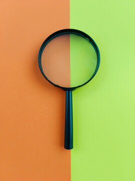 A magnifying glass isolated on a green and orange coloured background. Concept photography