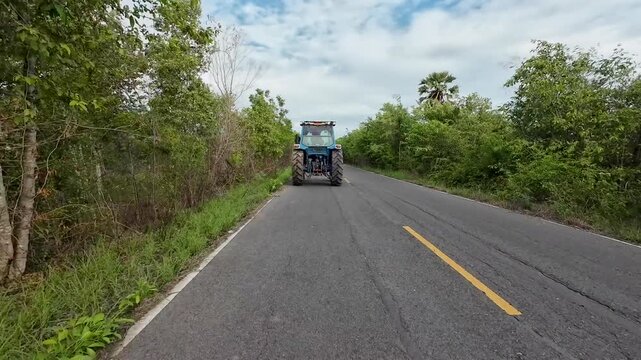 A large tractor is driving on a paved rural road.