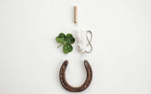 Lucky charms arrangement featuring four leaf clover vintage iron horseshoe and fuzzy rabbit foot on a clean white surface capturing traditional symbols of good fortune for a spiritual mystical concept