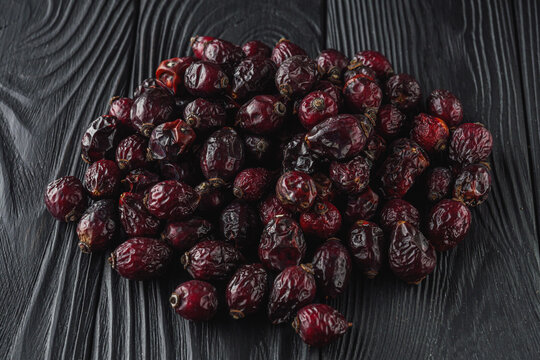 dried red rose hips on a black wooden rustic background