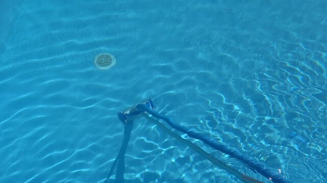 Underwater view of a vacuum cleaner head cleaning the bottom of a residential swimming pool on a sunny day