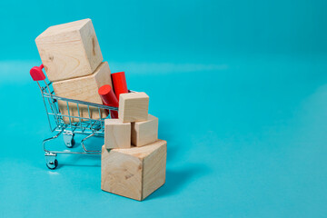 A small shopping cart filled with blank wooden blocks and stacked cubes on a vibrant blue background with copy space for text. High Quality Photo © 7TridentSea