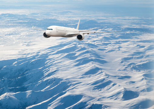 Passenger airplane flying over snowy mountains - White passenger airplane rising over amazing clouds