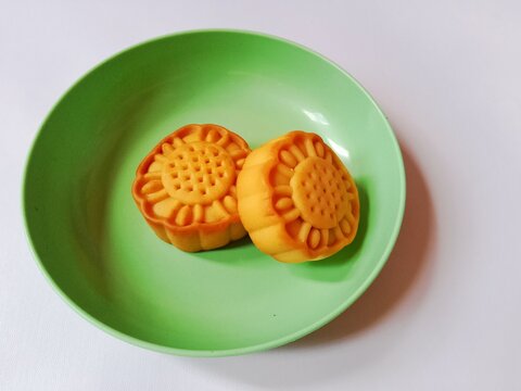 Two flower shaped baked cookies or mooncakes served in a light green plastic plate on a white table