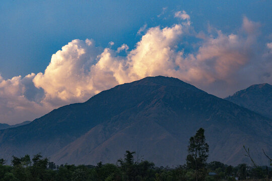 Mountain landscape in Nagri, Himachal Pradesh, India, with clouds illuminated by the setting sun standing out against the blue sky