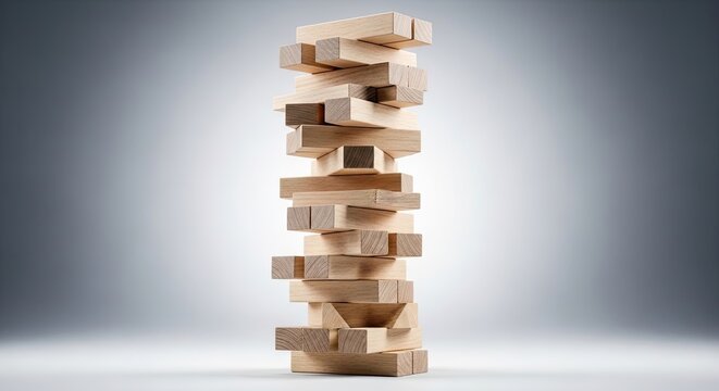 A tall, precarious stack of wooden blocks stands upright on a reflective surface. The blocks are arranged in a haphazard, unstable tower, creating a visually interesting composition.
