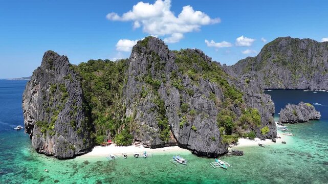 Smooth aerial drone footage moving backward and upward from a tropical beach surrounded by dramatic limestone karst cliffs in El Nido, Palawan, Philippines. The cinematic pullback gradually reveals th