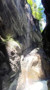 Sunlight highlights a steep canyon wall with a trickling waterfall pouring into a fast mountain river