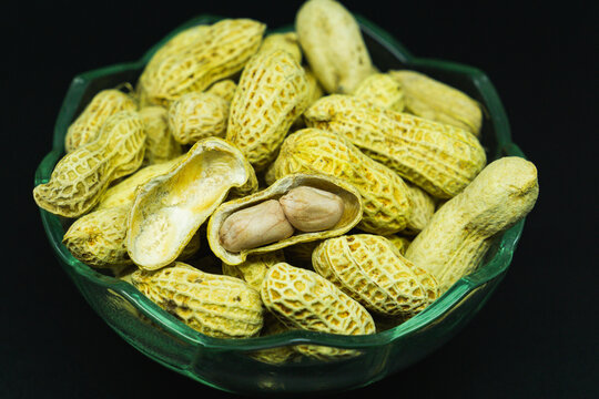 Peanuts sit in a glass bowl. Dark background highlights their natural texture. They look fresh, unpeeled, and untouched. Ideal for food, health, or rustic cooking themes. No people, no animals.