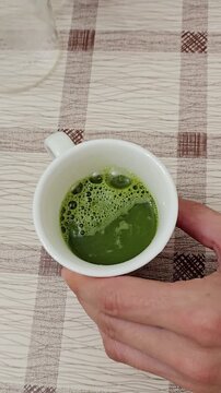 Homemade matcha tea being whisked in a white cup, showing the process of pouring water and mixing green matcha powder into a smooth frothy drink